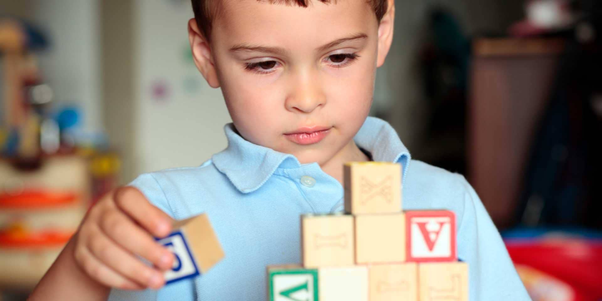 A young boy in a school uniform is stacking wooden blocks.