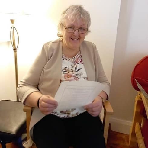National Advocacy Representative Nora Healy. Nora is sitting in a chair smiling and holding a sheet of paper in her hands.