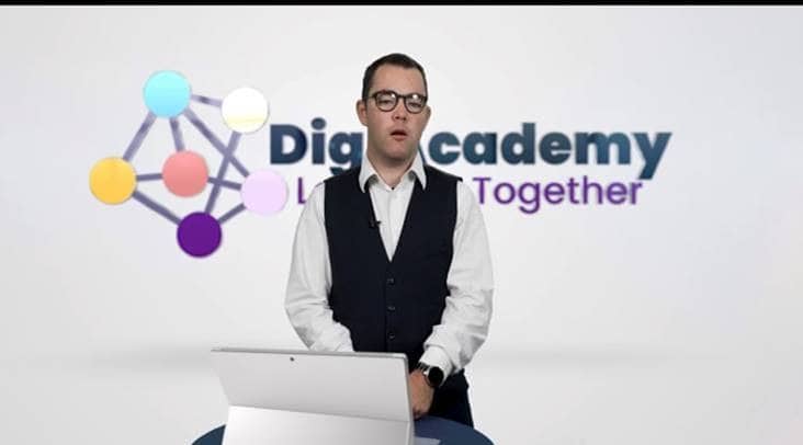 A man giving a presentation posing in front of a screen that reads "Digiacademy"